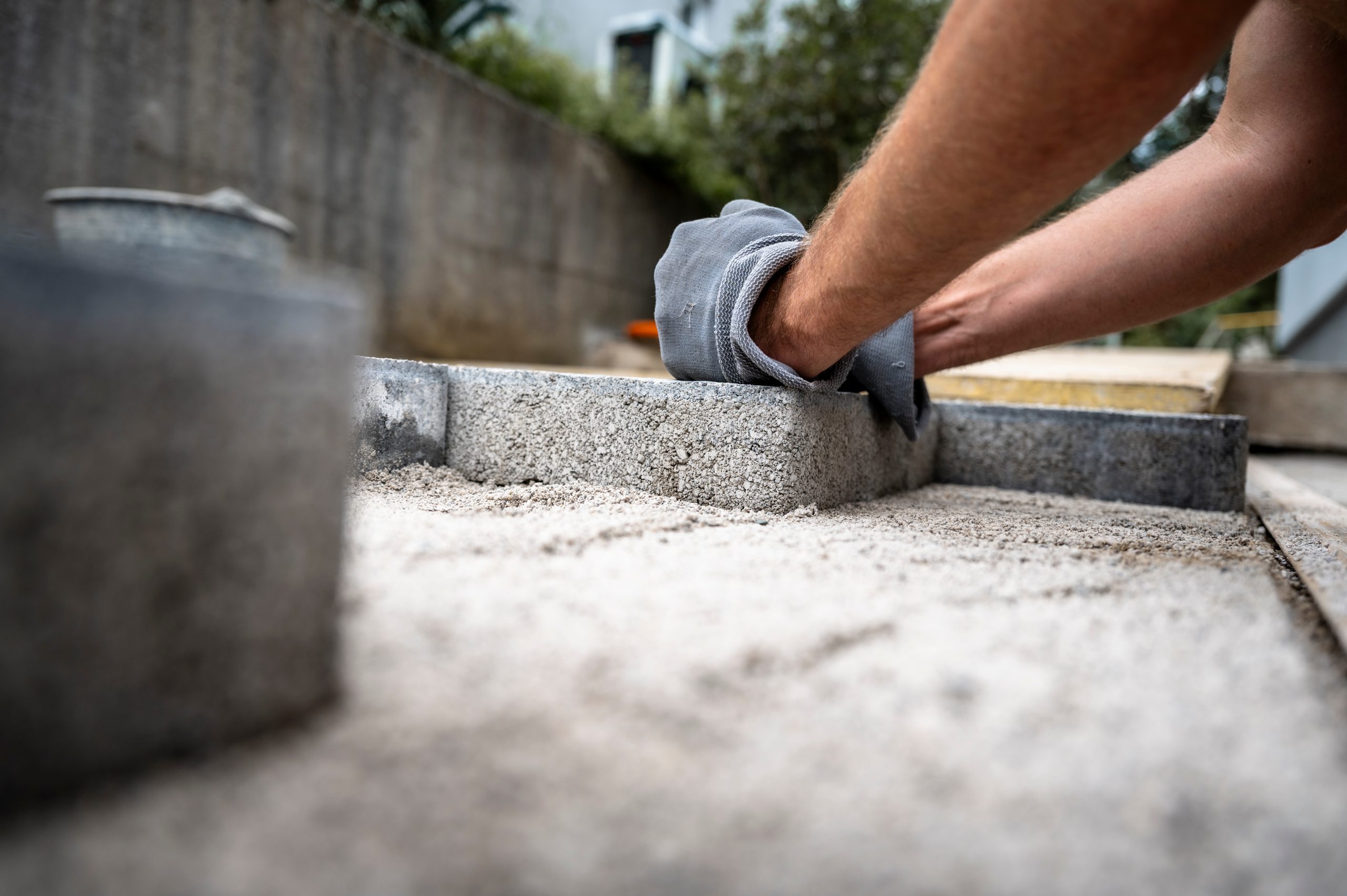 Closeup of a person wearing gloves carefully placing concrete pavers on a sandy base during a patio construction project.