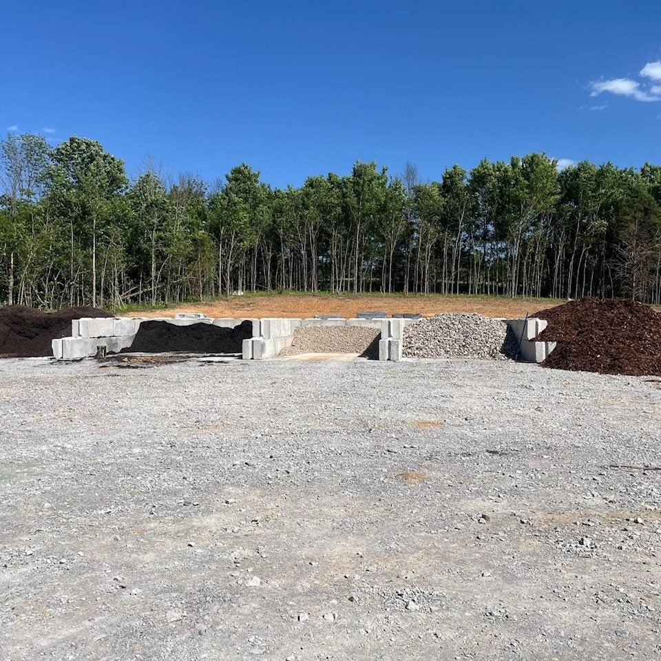 Gravel and soil piles at a construction site with trees in the background.
